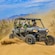 2 riders wearing helmets riding a 4 by 4 all terrain vehicle through the desert
